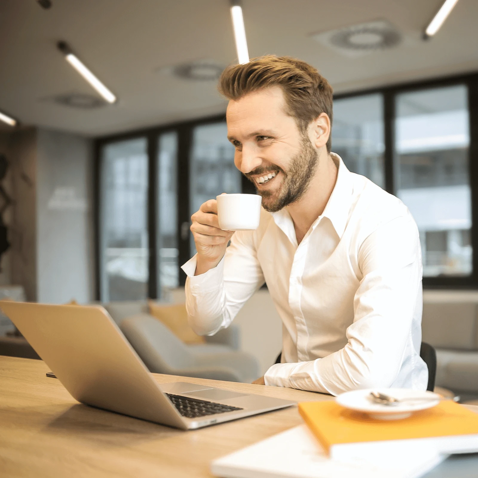 Man working at this desk while sipping tea and smiling